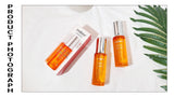 Three orange skincare bottles with silver caps on a white background with a green leaf.